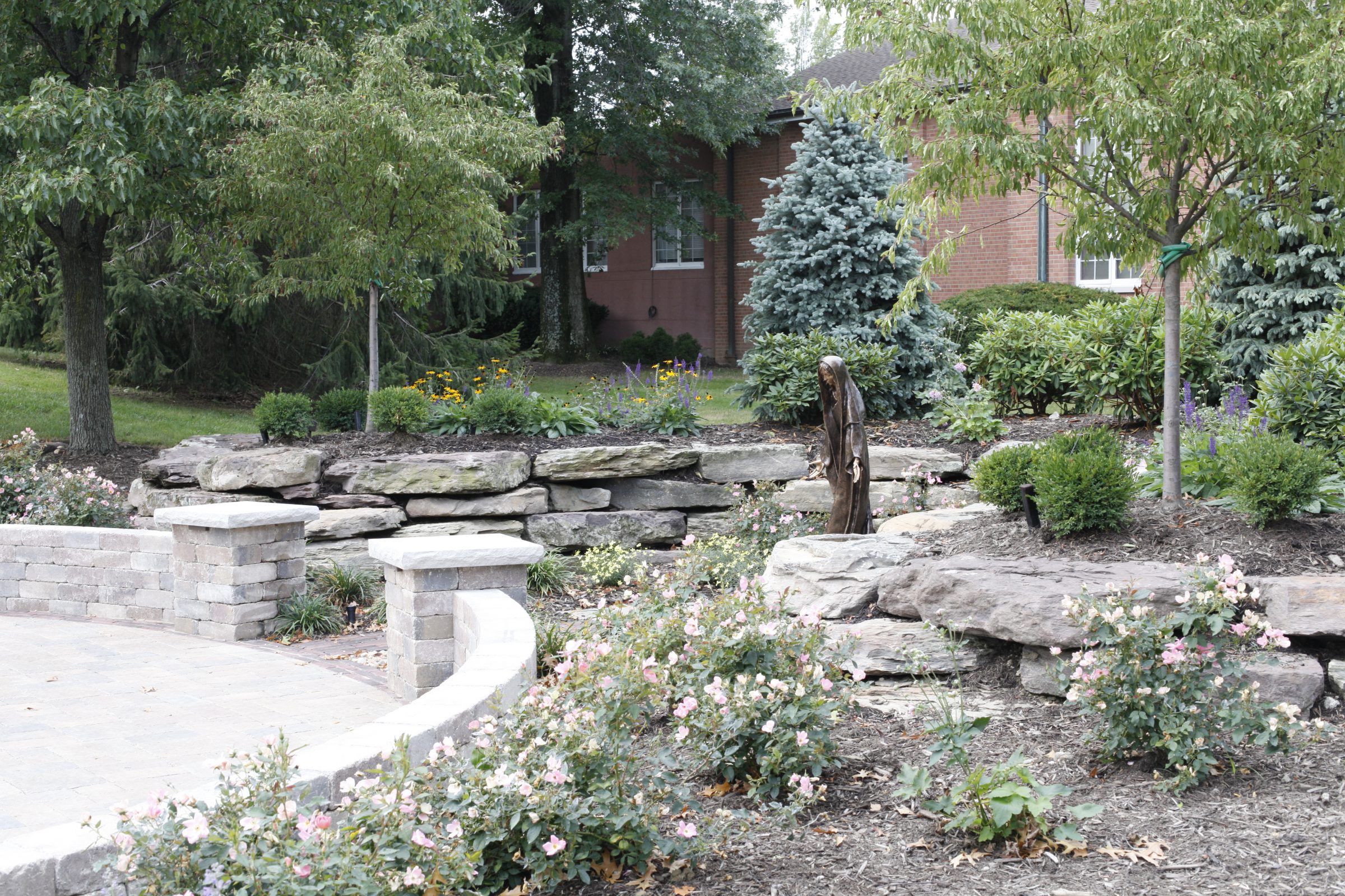 Garden with statue, flowers, and stone wall.