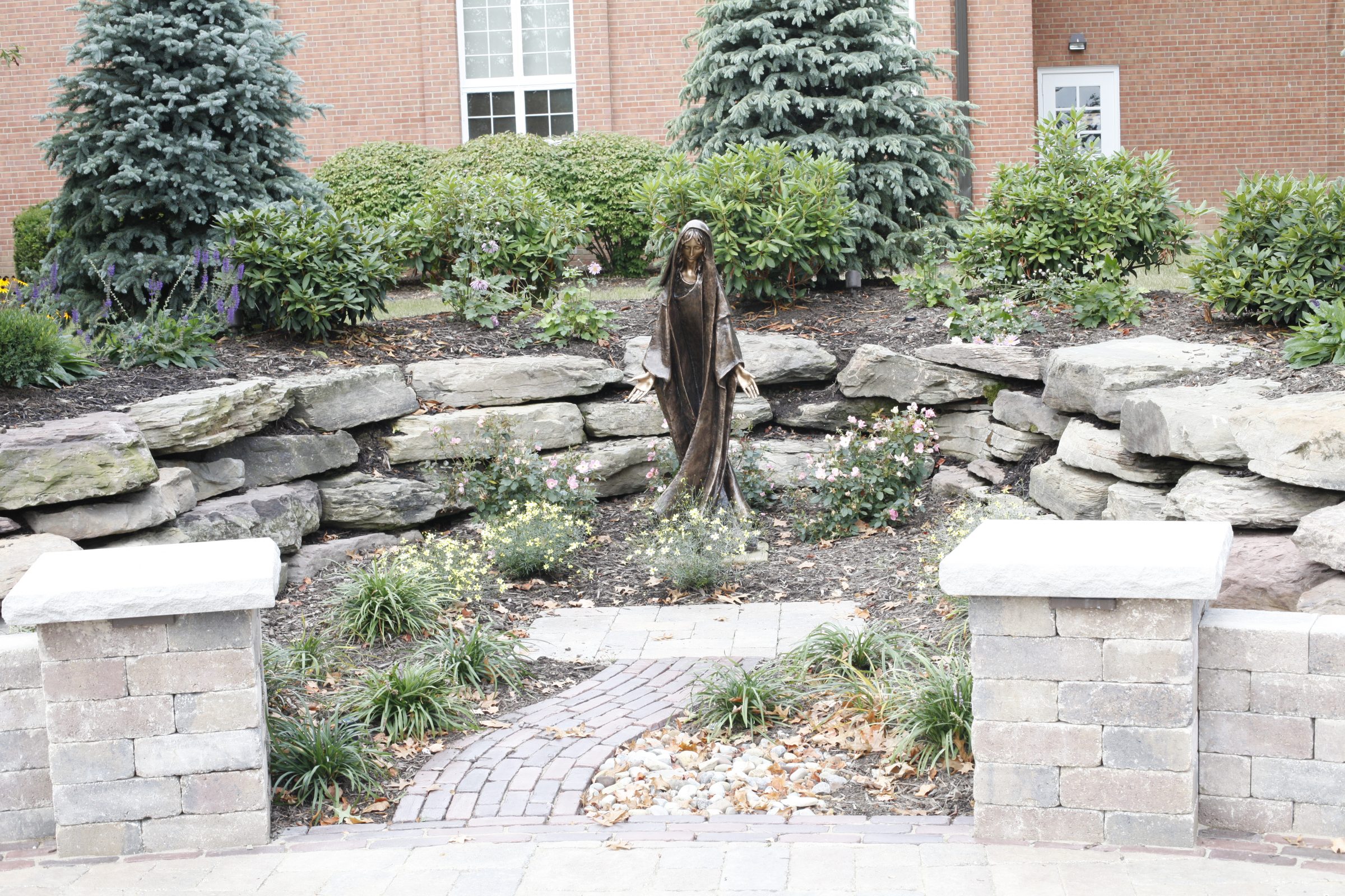 Statue in garden with stone wall and plants.