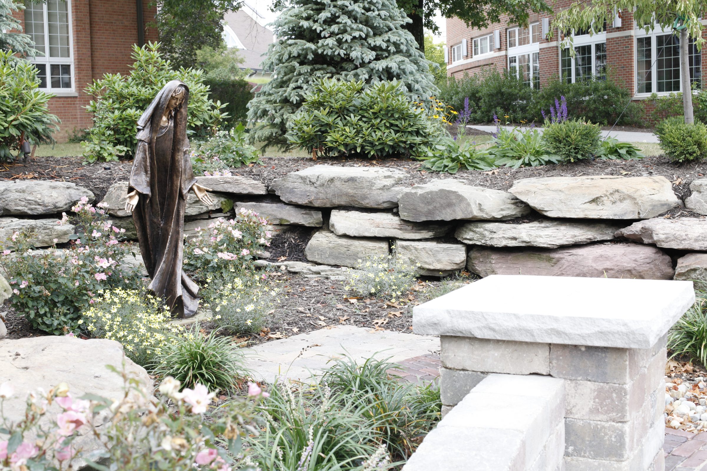 Garden statue surrounded by flowers and stone wall