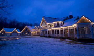 Snow-covered house at dusk with Christmas lights.