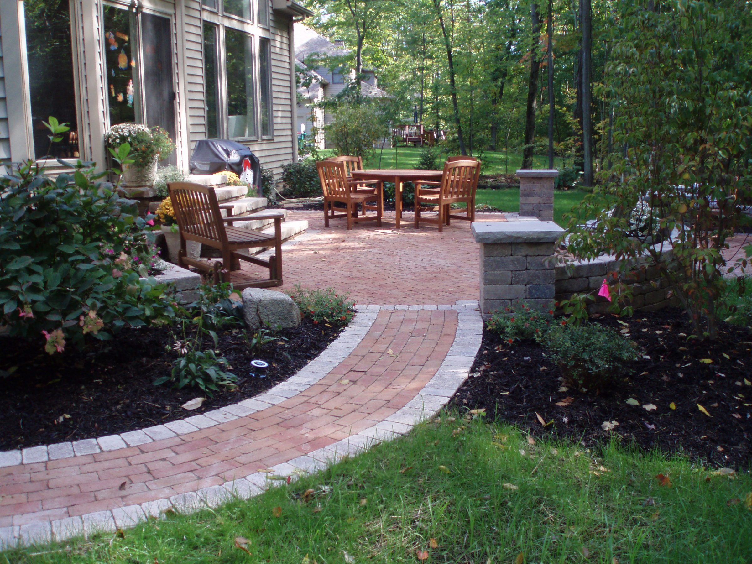 Brick patio with wooden chairs and garden view.