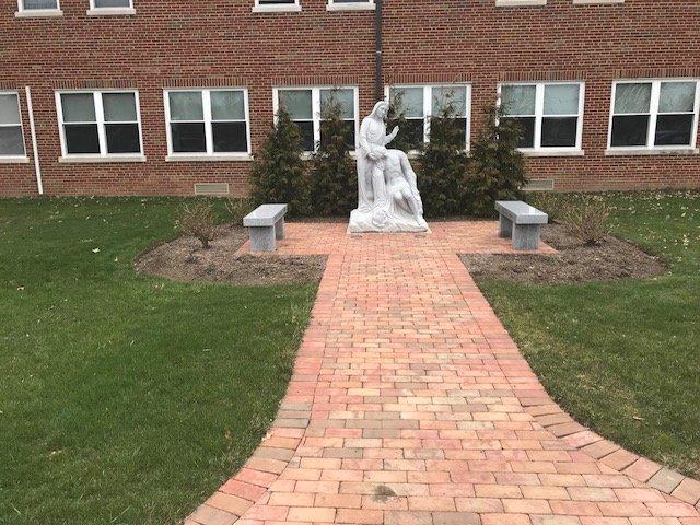 Brick path to statue and benches in garden.