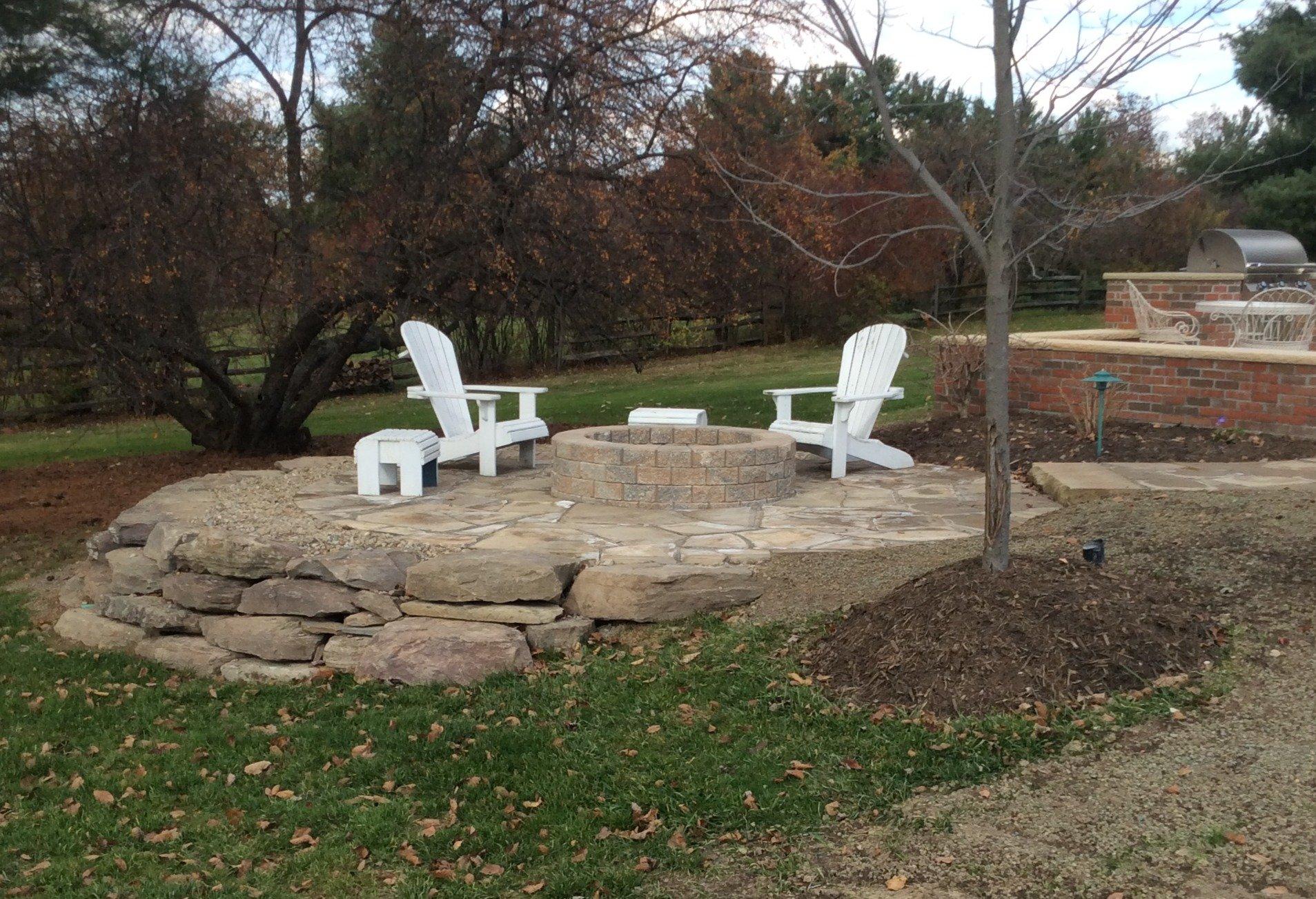 Outdoor fire pit with white chairs in backyard