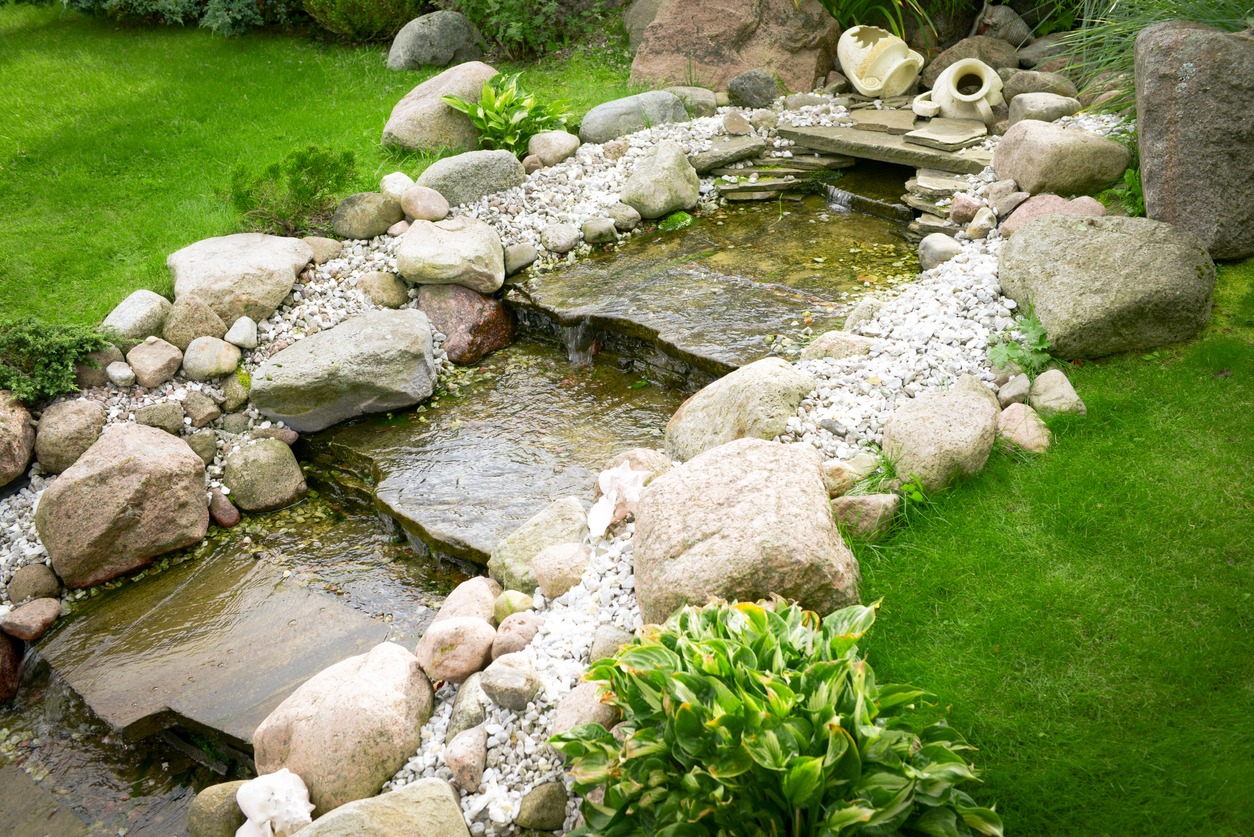 Tranquil garden stream with rocks and plants.