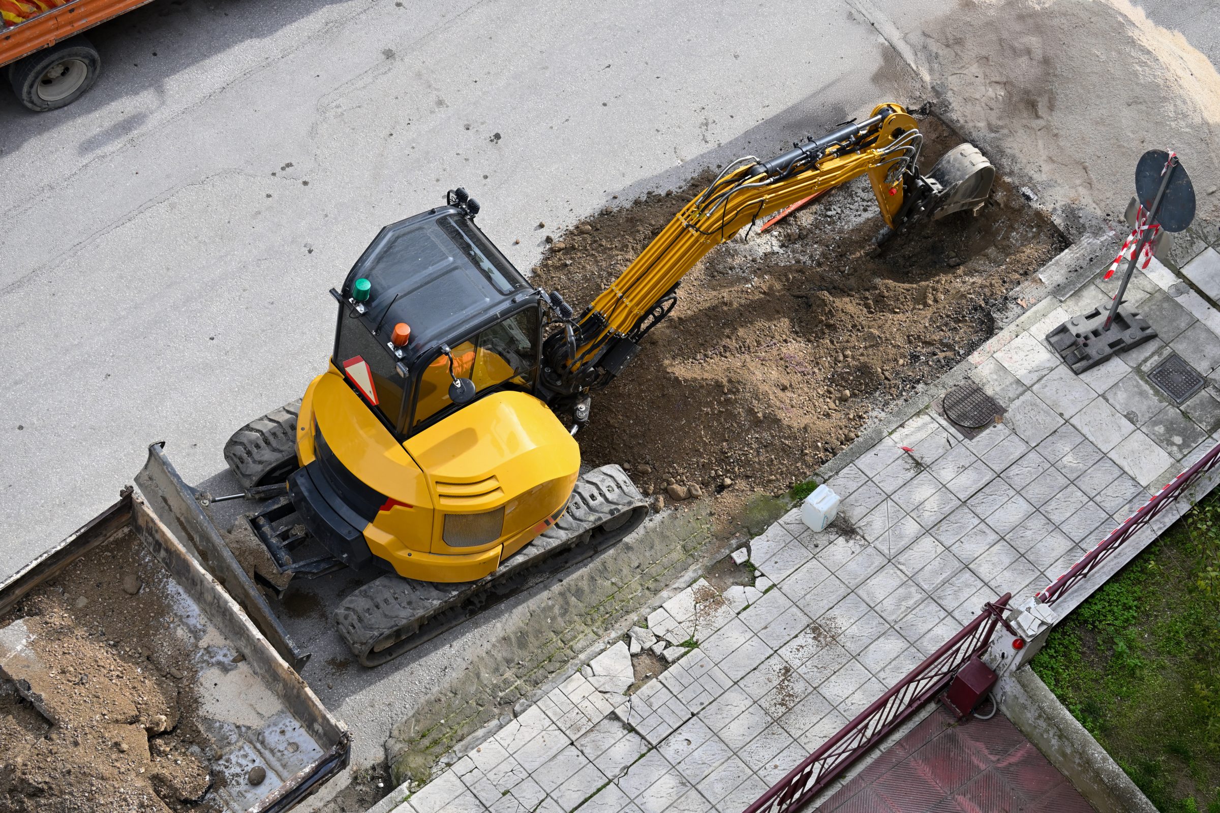 Yellow excavator digging road near sidewalk