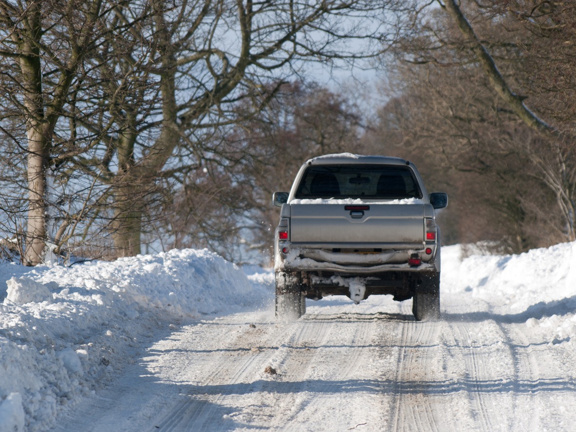 Truck driving on snowy rural road.