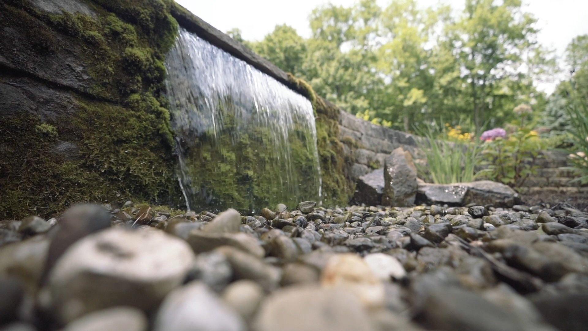 Waterfall with stones and lush greenery backdrop.